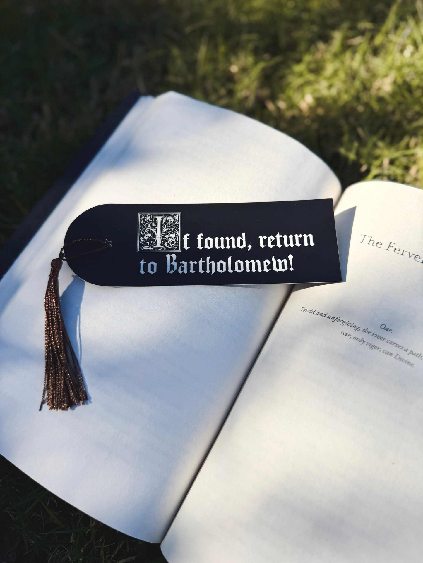 The Foulest Reader Bookmark is black and white and lies on a book outdoors. It reads "If found, return to Bartholomew" and is inspired by the book The Knight and the Moth by Rachel Gillig.