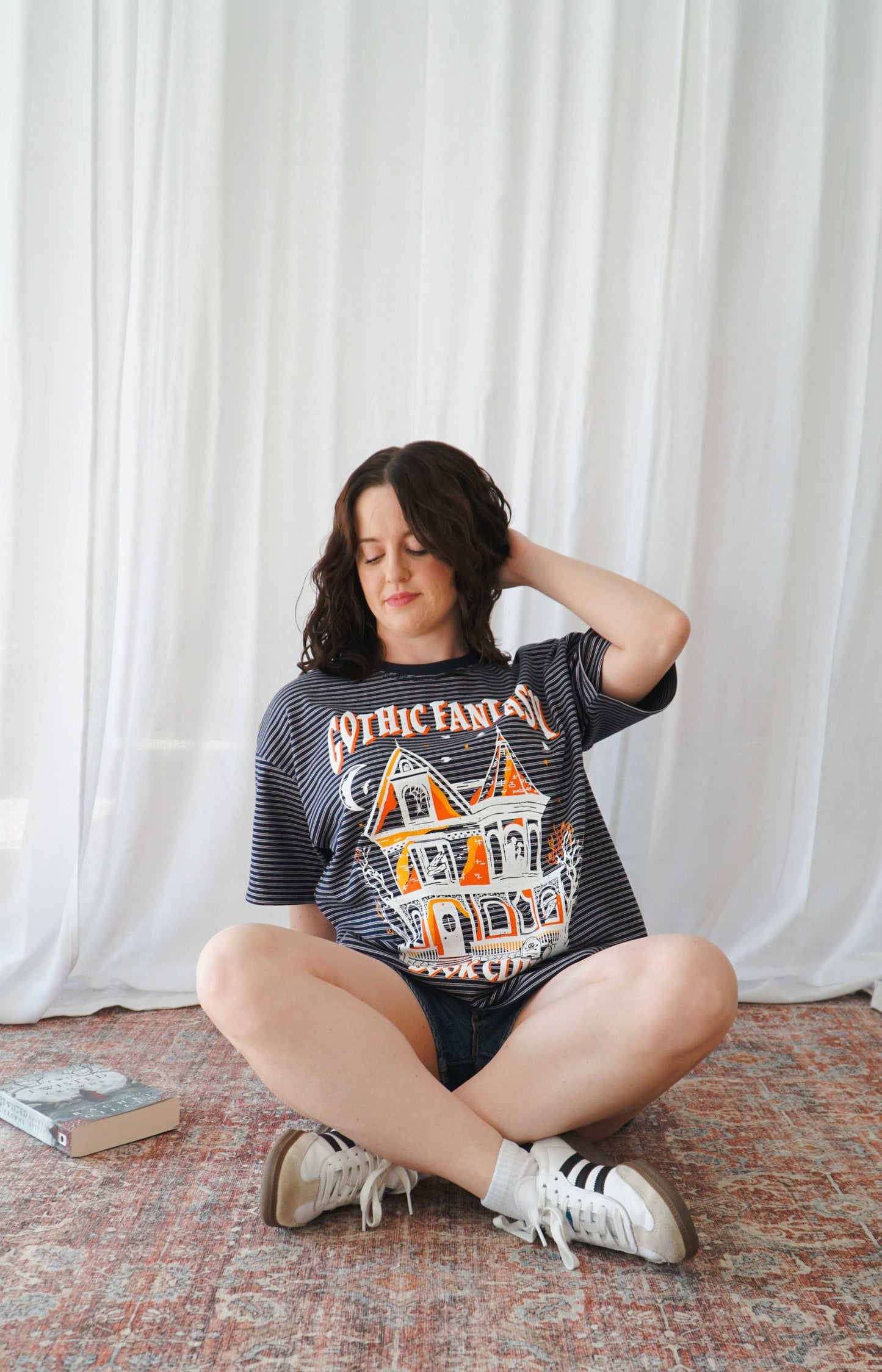 Person wearing a graphic t-shirt sitting on the floor against a white curtain. Striped oversized boxy Gothic Fantasy Tee / t-shirt. For book lovers of the romantasy genre.