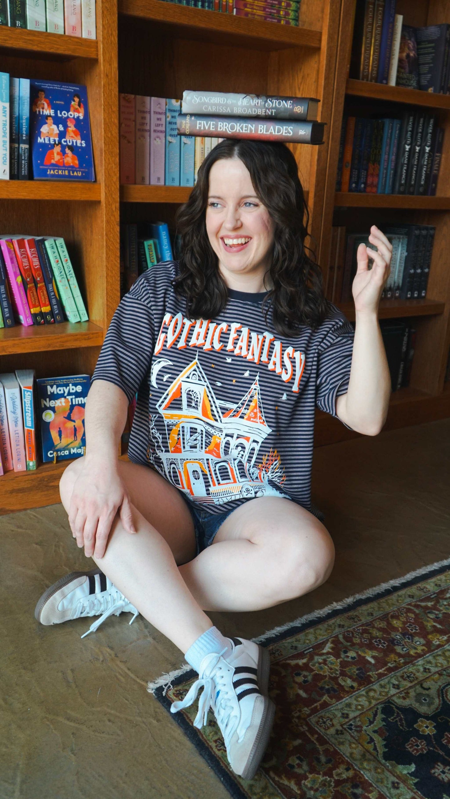 Woman sitting on the floor in front of a bookshelf wearing a 'Gothic Fantasy' t-shirt. Striped oversized boxy Gothic Fantasy Tee / t-shirt. For book lovers of the romantasy genre.