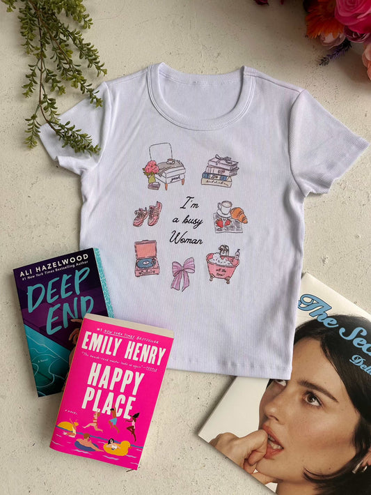 Busy Woman Tee. A slim fit ribbed tee inspired by books, music, feminine hobbies, and the Sabrina Carpenter song Busy Woman is featured with the books Deep End and Happy Place. A super soft bookish summer t-shirt that is perfect for the bookstagram girls and the booked and busy fangirls.