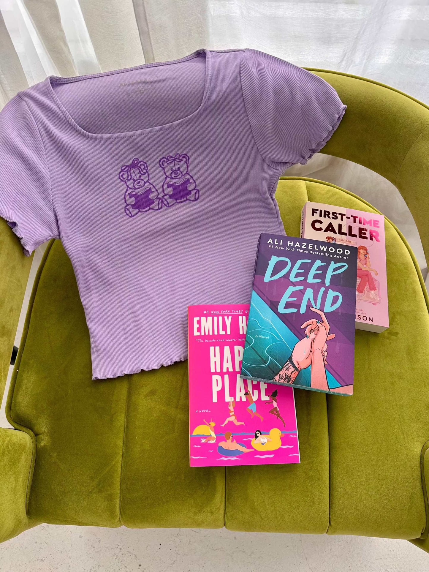 The Book Bears Baby Tee features a design with two teddy bears each holding a book. The t-shirt is a light purple color with a deep purple bookish design and lettuce hem trim.