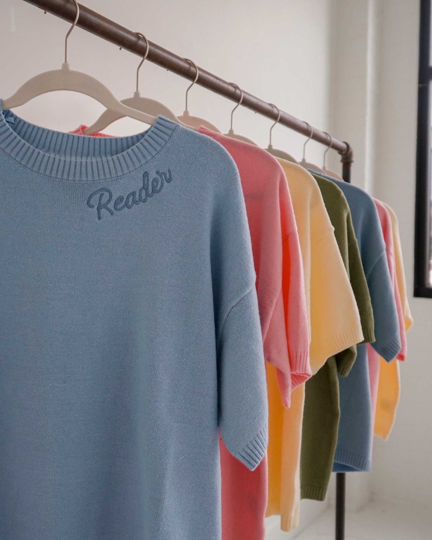 Cozy Reader Knit Sweater for book lovers on a hanger against a plain background. The sweater has the word 'reader' embroidered along the collar.