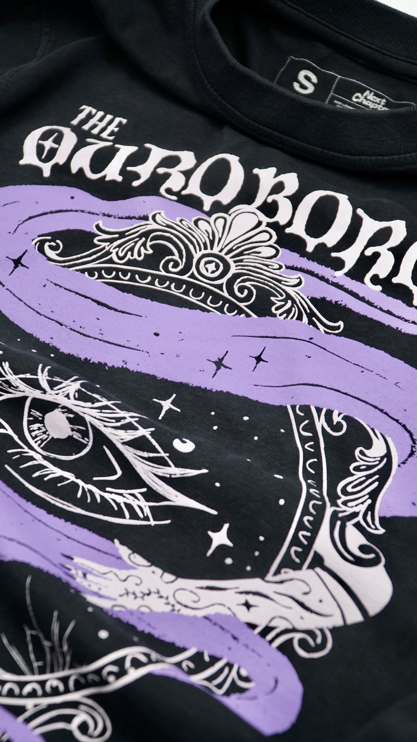 Black t-shirt with white and purple designs and 'The Ouroboros' text. A black graphic tee with 'The Ourororos' design featuring an eye, mirror, and purple mist. Inspired by the A Court of Thorns of Roses book series by Sarah J. Maas.