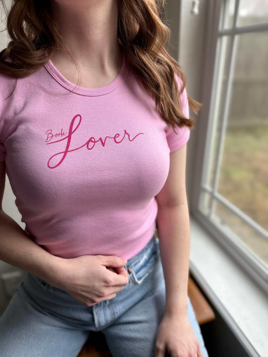 Pink ribbed cotton Book Lover Baby Tee with vibrant screen print worn by model sitting near window