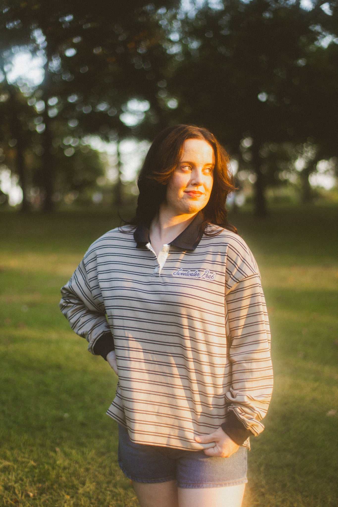 Woman wearing a striped shirt with a Sweetwater Peak logo in a park setting. She is wearing a Sweetwater Peak Rugby Top inspired by the book Soul Searching by Lyla Sage. Officially licensed by Lyla Sage.
