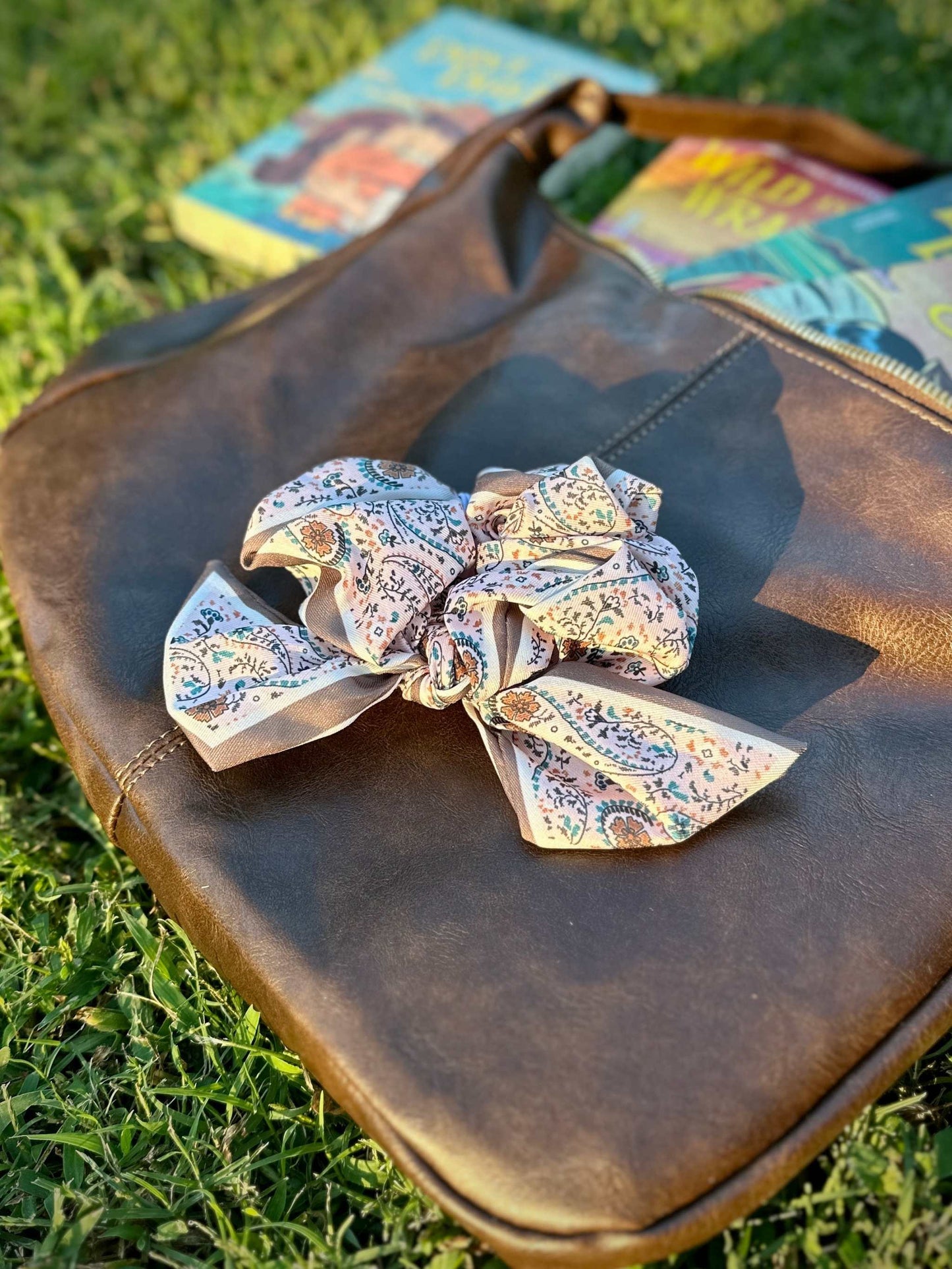 Pink paisley Clementine Scrunchie on brown leather bag outdoors. Inspired by Lyla Sage's cowboy romance book series.