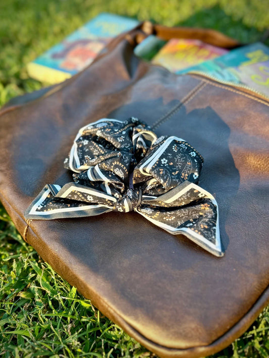Black paisley Clementine Scrunchie on brown leather bag outdoors. Inspired by Lyla Sage's cowboy romance book series.