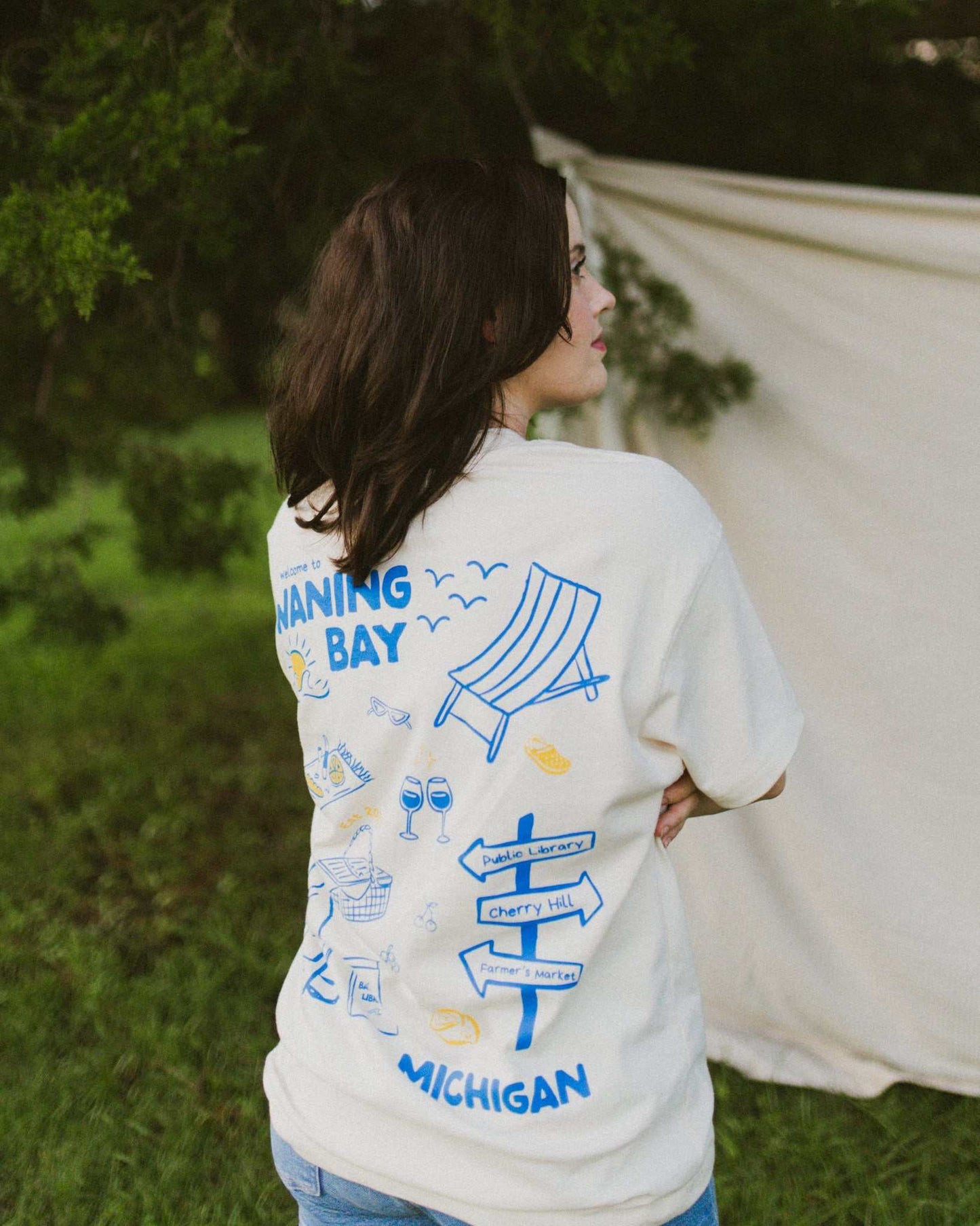 An oversized, boxy t-shirt, the Funny Story Tee is inspired by the book Funny Story by Emily Henry. The item is an ivory/cream color with a royal blue and gold design on the front and back.