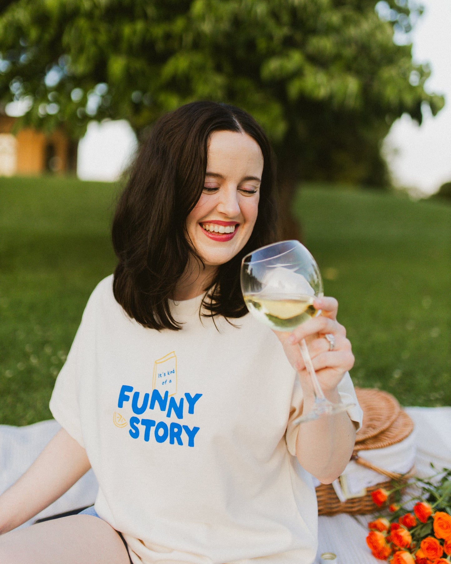 An oversized, boxy t-shirt, the Funny Story Tee is inspired by the book Funny Story by Emily Henry. The item is an ivory/cream color with a royal blue and gold design on the front and back.