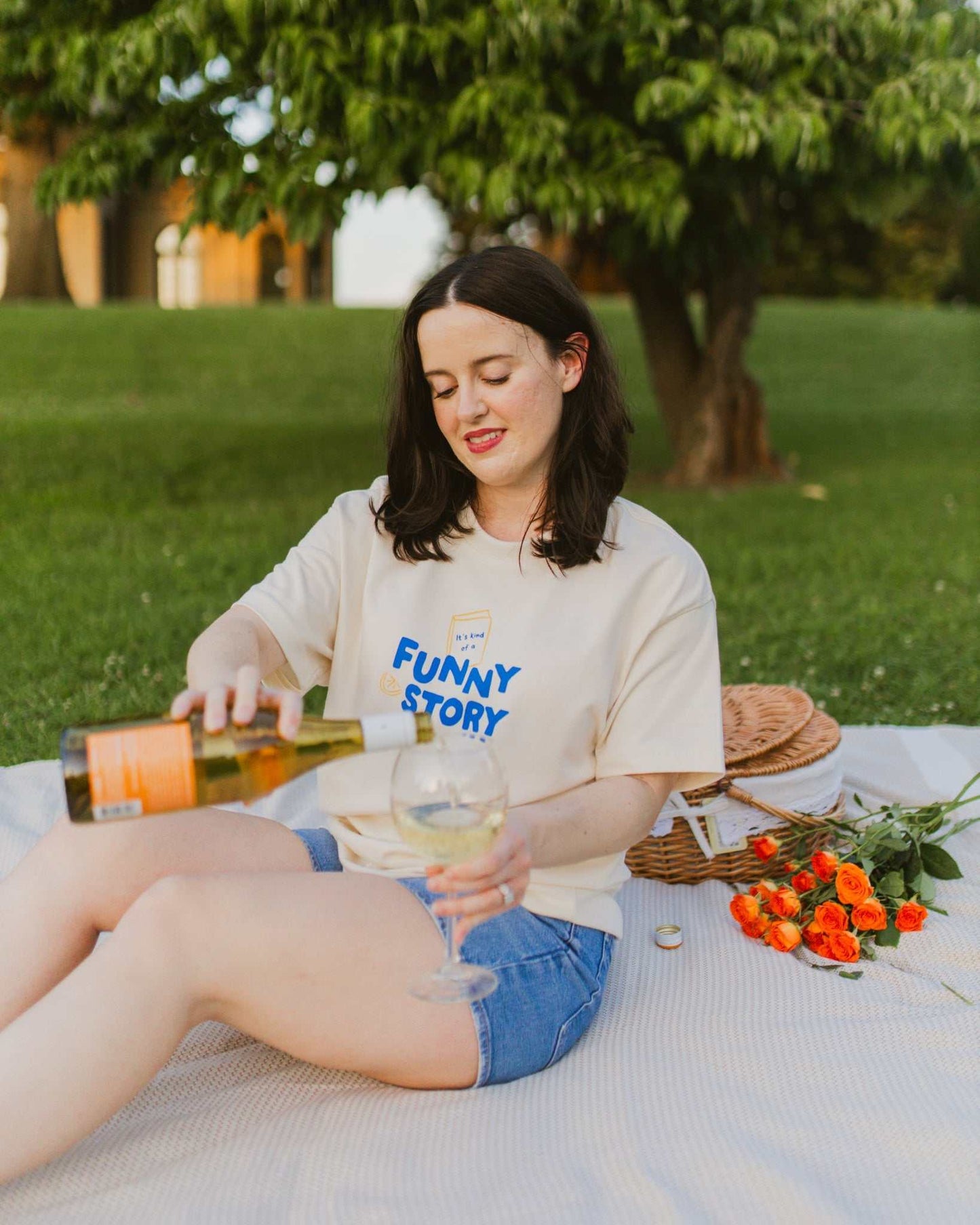 An oversized, boxy t-shirt, the Funny Story Tee is inspired by the book Funny Story by Emily Henry. The item is an ivory/cream color with a royal blue and gold design on the front and back.