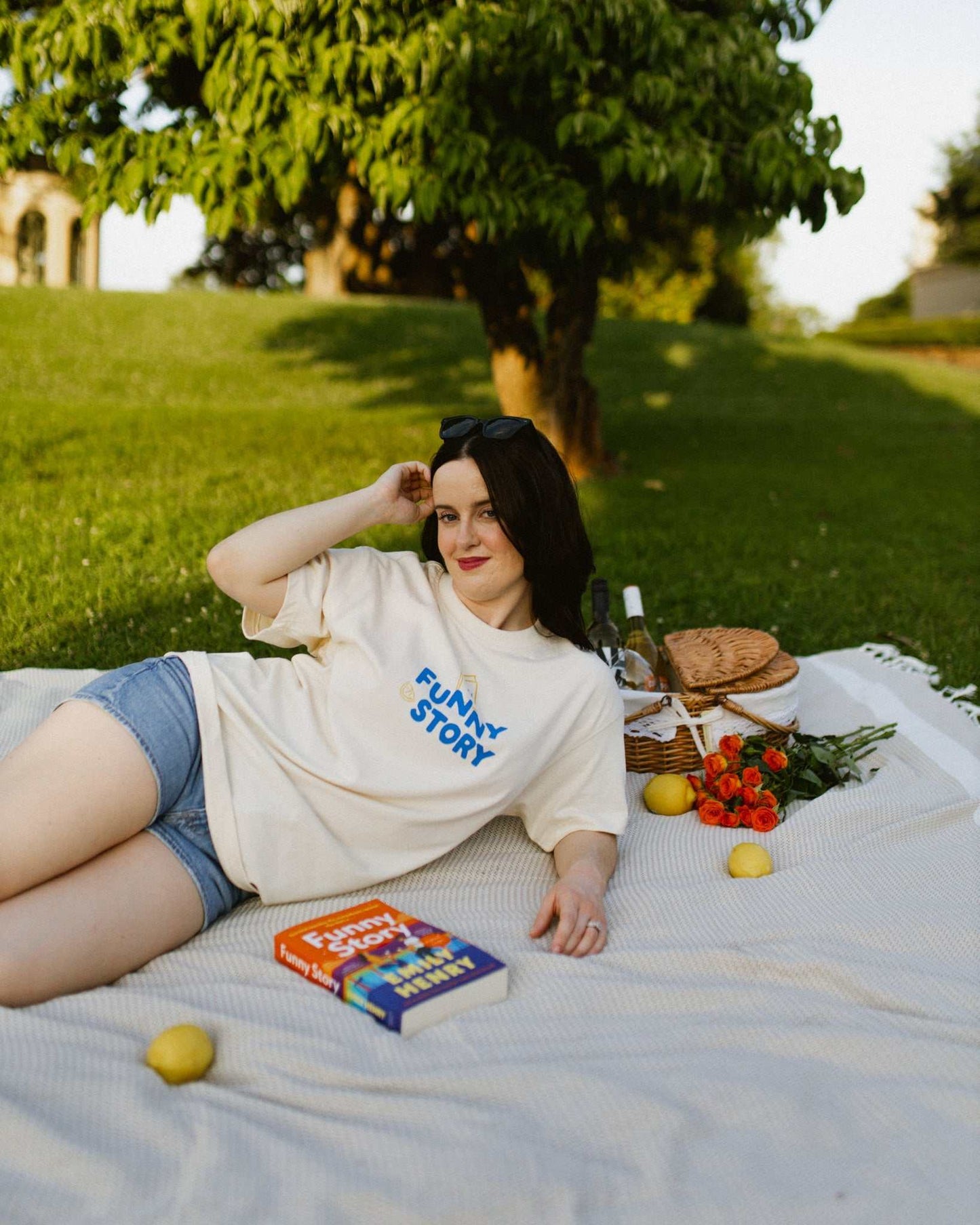 An oversized, boxy t-shirt, the Funny Story Tee is inspired by the book Funny Story by Emily Henry. The item is an ivory/cream color with a royal blue and gold design on the front and back.