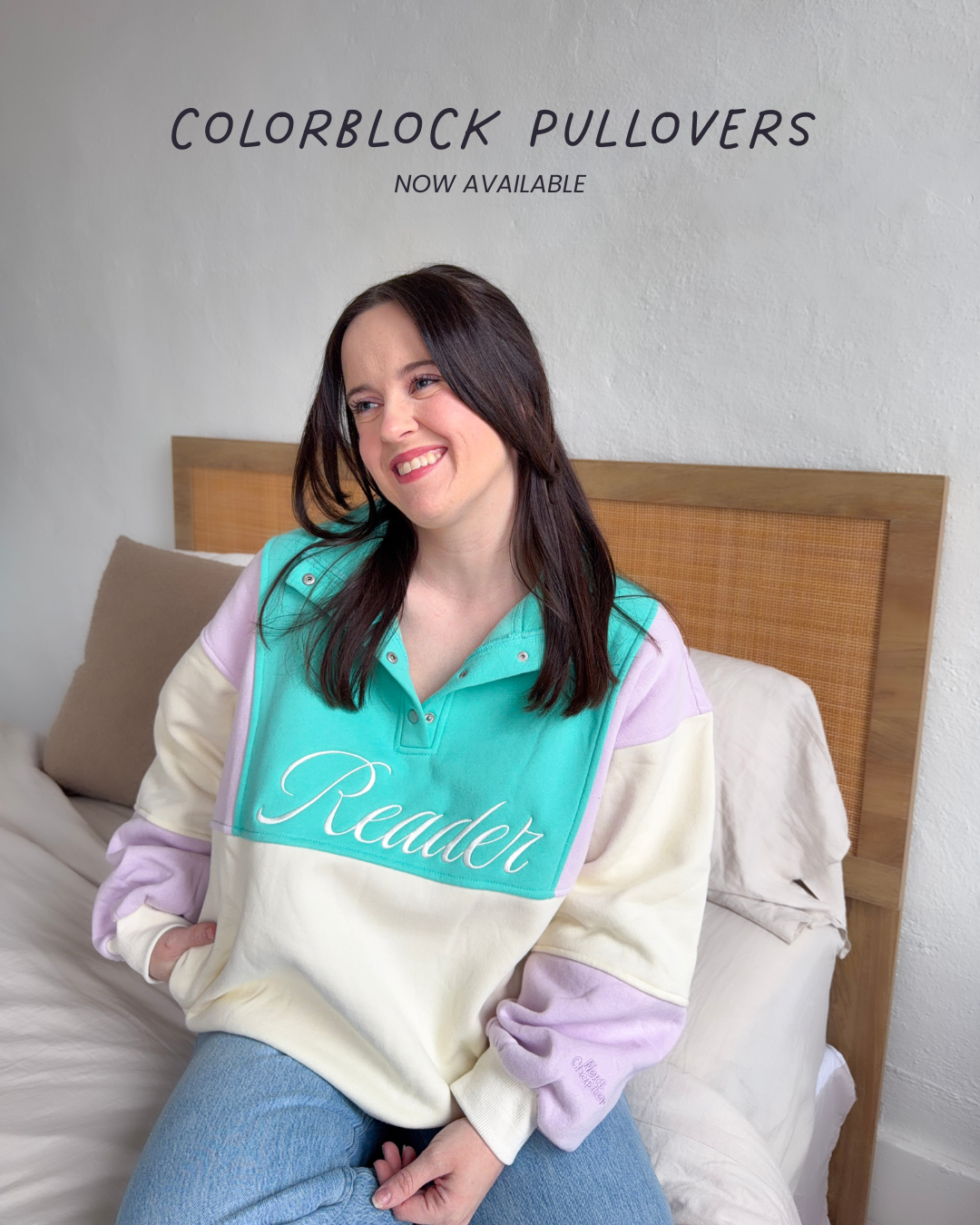 Woman wearing a colorblock sweater with 'Reader' text, sitting on a bed with text on the image that says 'now available'