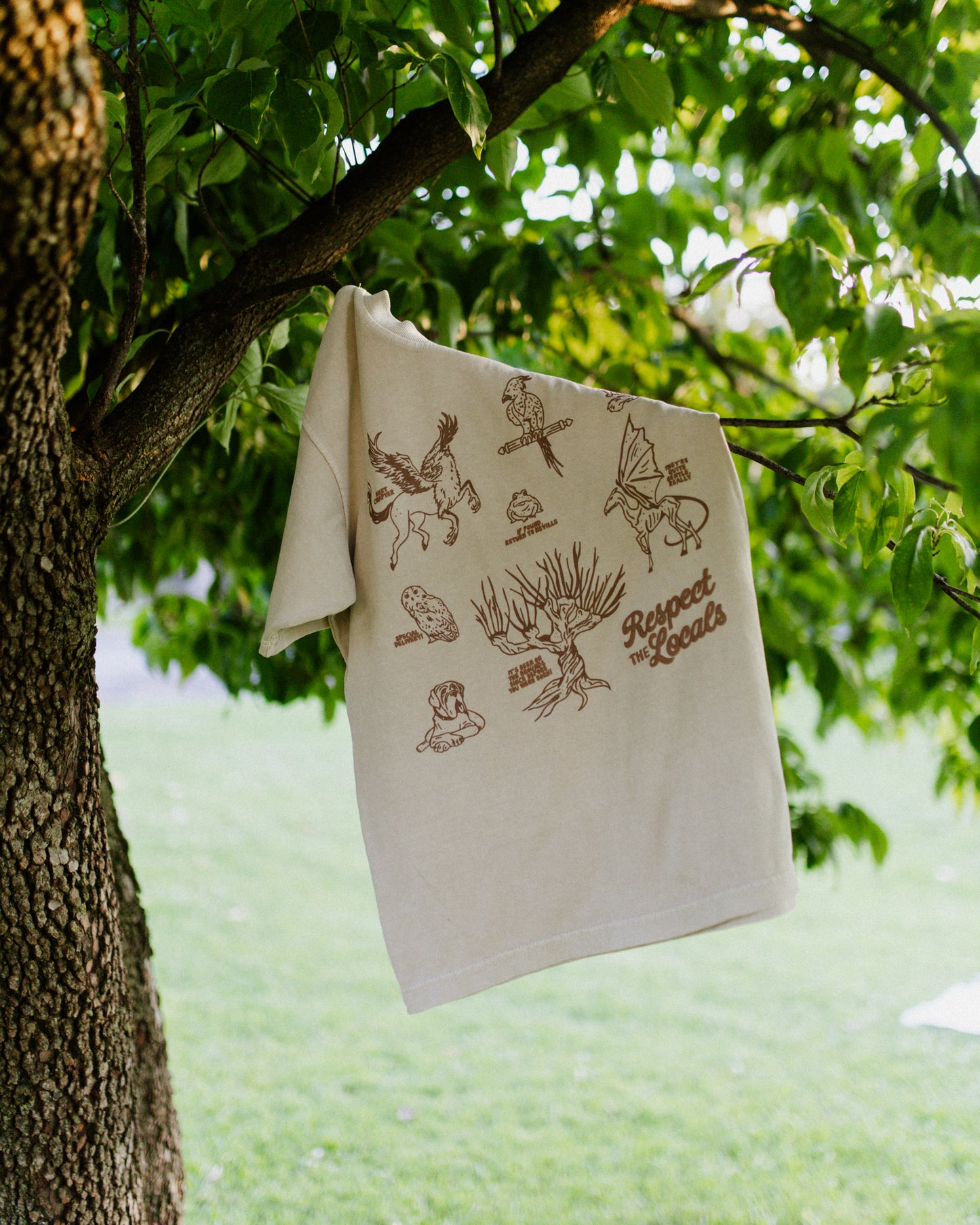 Beige t-shirt with a brown design depicting creatures from Harry Potter hanging from a tree.