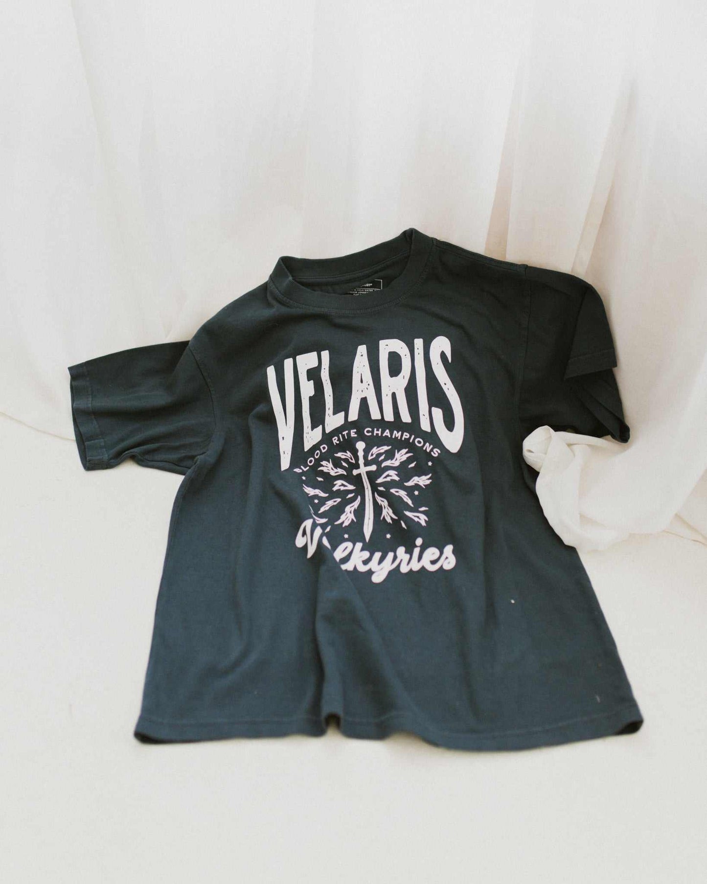 Velaris Valkyries tee featuring a deep navy fabric and white, screen printed design. From A Court of Silver Flames. Officially licensed by Sarah J. Maas.
