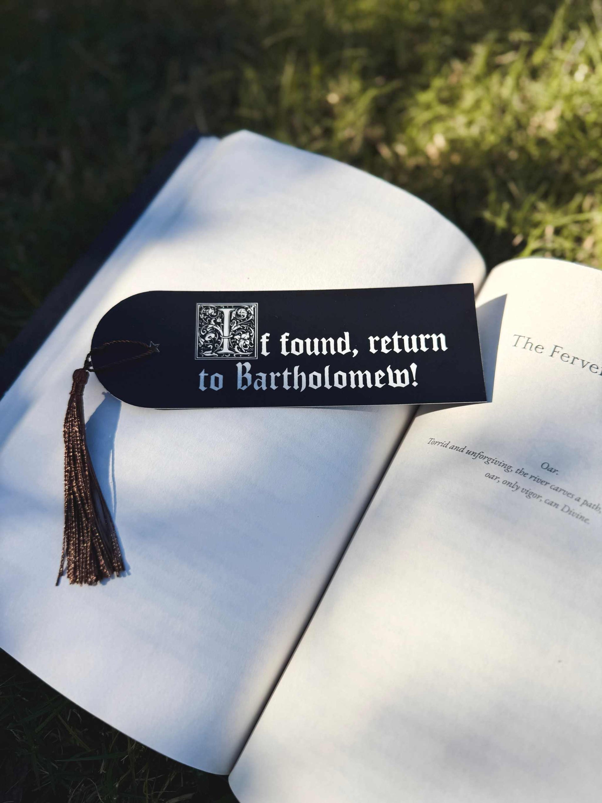 The Foulest Reader Bookmark is black and white and lies on a book outdoors. It reads "If found, return to Bartholomew" and is inspired by the book The Knight and the Moth by Rachel Gillig. 