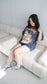 Woman sitting on a white couch wearing a graphic t-shirt and denim shorts. Striped oversized boxy Gothic Fantasy Tee / t-shirt. For book lovers of the romantasy genre. 
