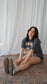 Woman sitting on a patterned rug with white curtains in the background. Striped oversized boxy Gothic Fantasy Tee / t-shirt. For book lovers of the romantasy genre. 