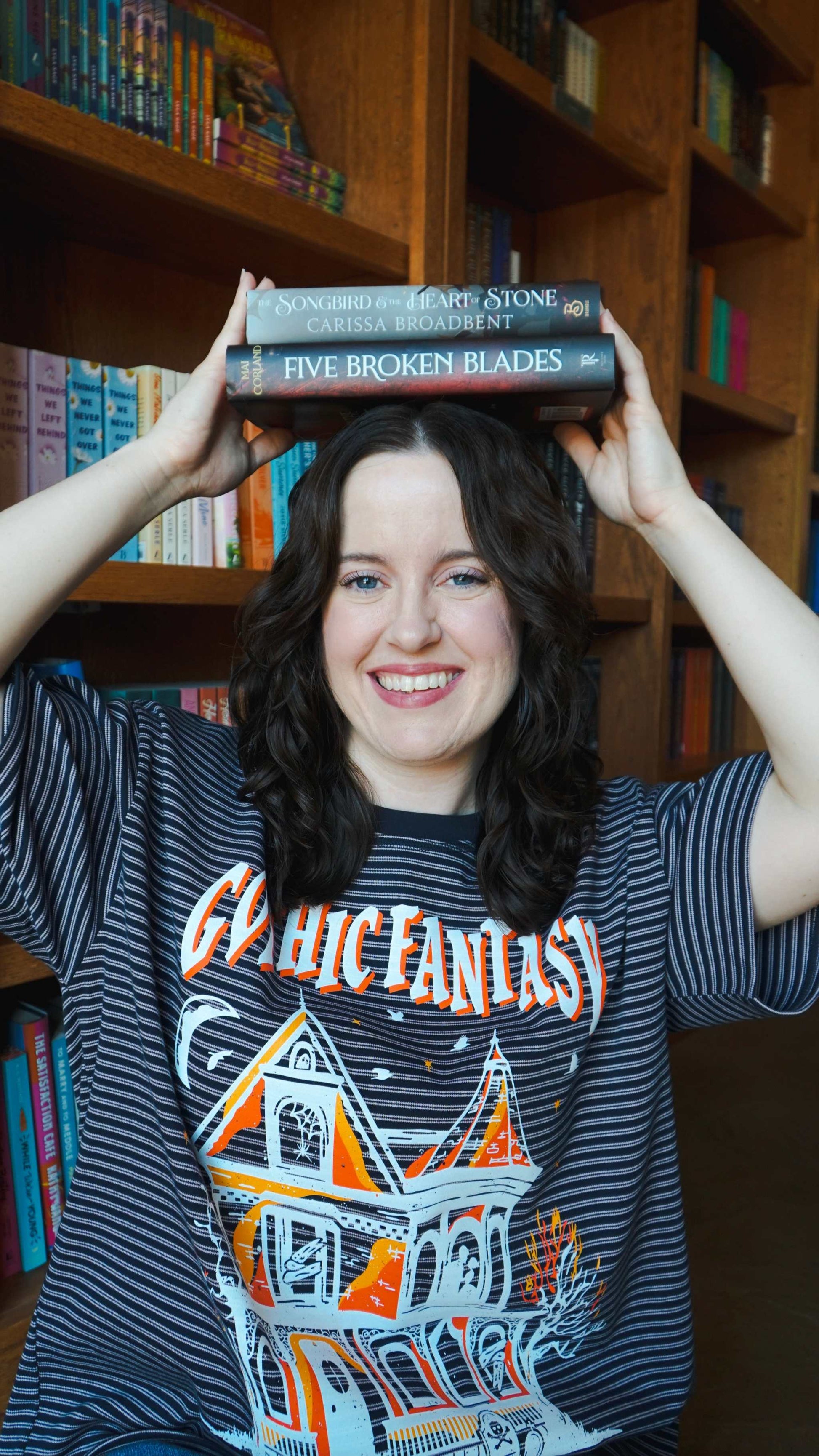 Person holding books on their head with a bookshelf in the background. Striped oversized boxy Gothic Fantasy Tee / t-shirt. For book lovers of the romantasy genre. 
