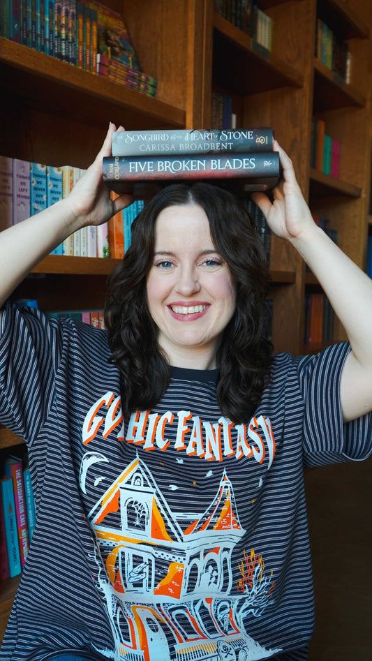 Person holding books on their head with a bookshelf in the background. Striped oversized boxy Gothic Fantasy Tee / t-shirt. For book lovers of the romantasy genre.