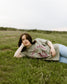 Rebel Blue Ranch Mustangs Tee. A woman wears a mineral wash olive green boxy oversized Rebel Blue Ranch tee with a horses design based on the cowboy romance book series by Lyla Sage that includes Done and Dusted, Swift and Saddled, Lost and Lassoed, and Wild and Wrangled. Meadowlark bookish merch. Lyla Sage merch.