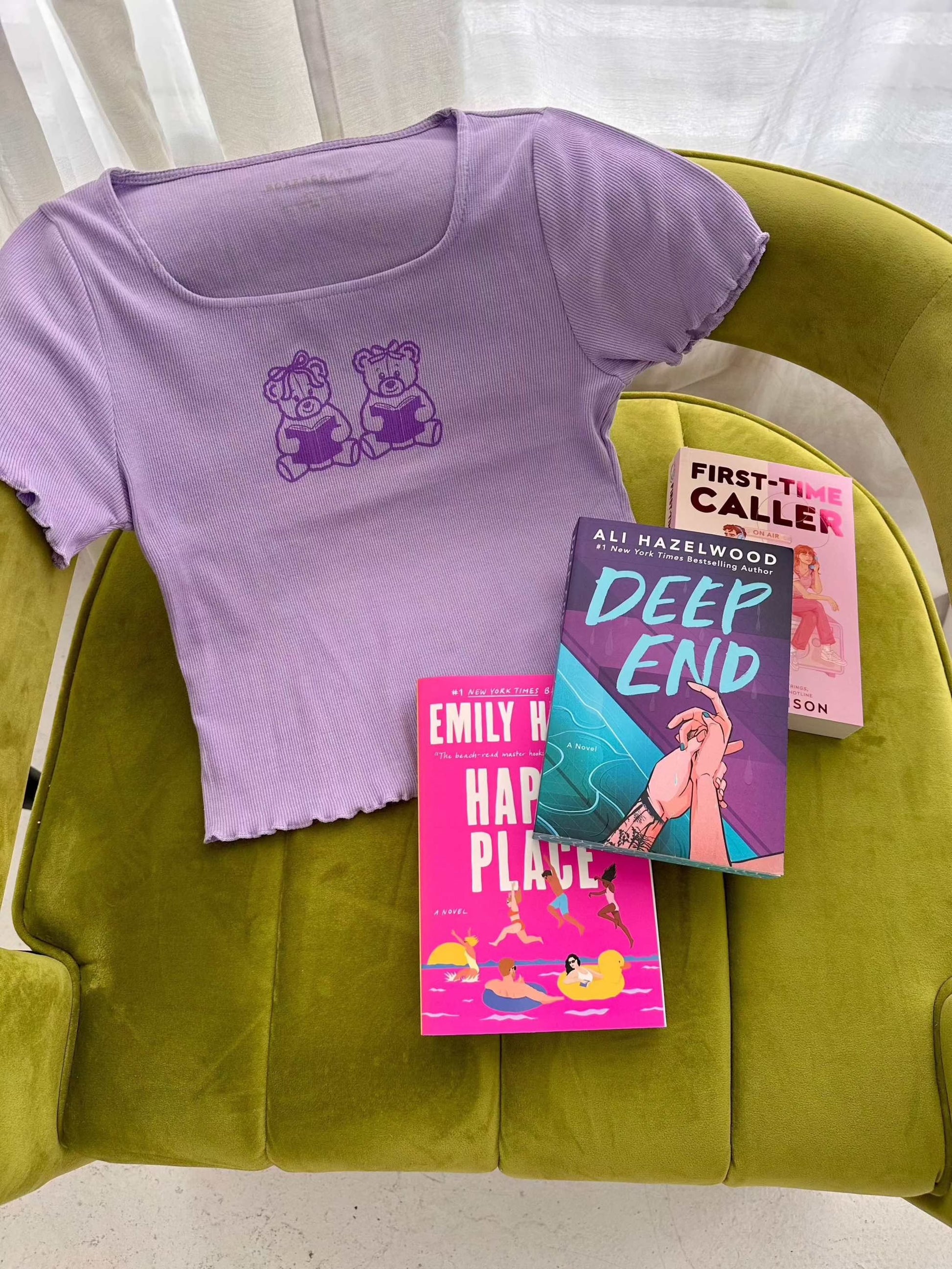 The Book Bears Baby Tee features a design with two teddy bears each holding a book. The t-shirt is a light purple color with a deep purple bookish design and lettuce hem trim.