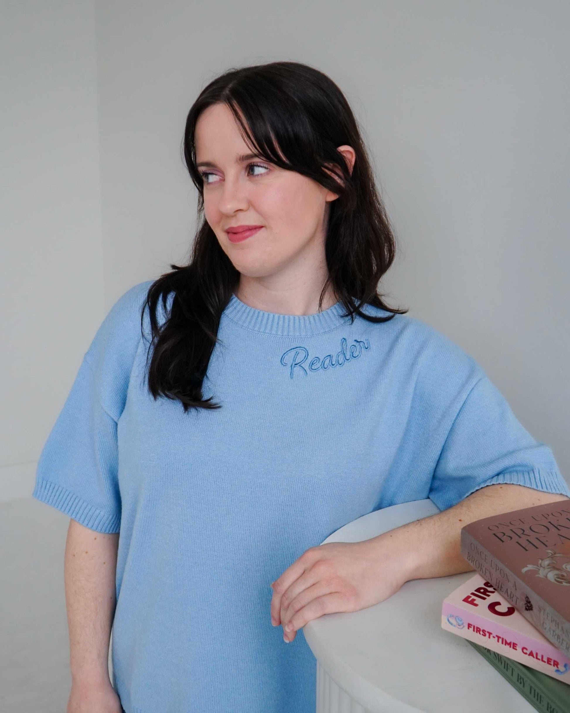 Woman wearing a cozy blue Reader Knit Sweater for book lovers with 'reader' embroidered along the collar. 