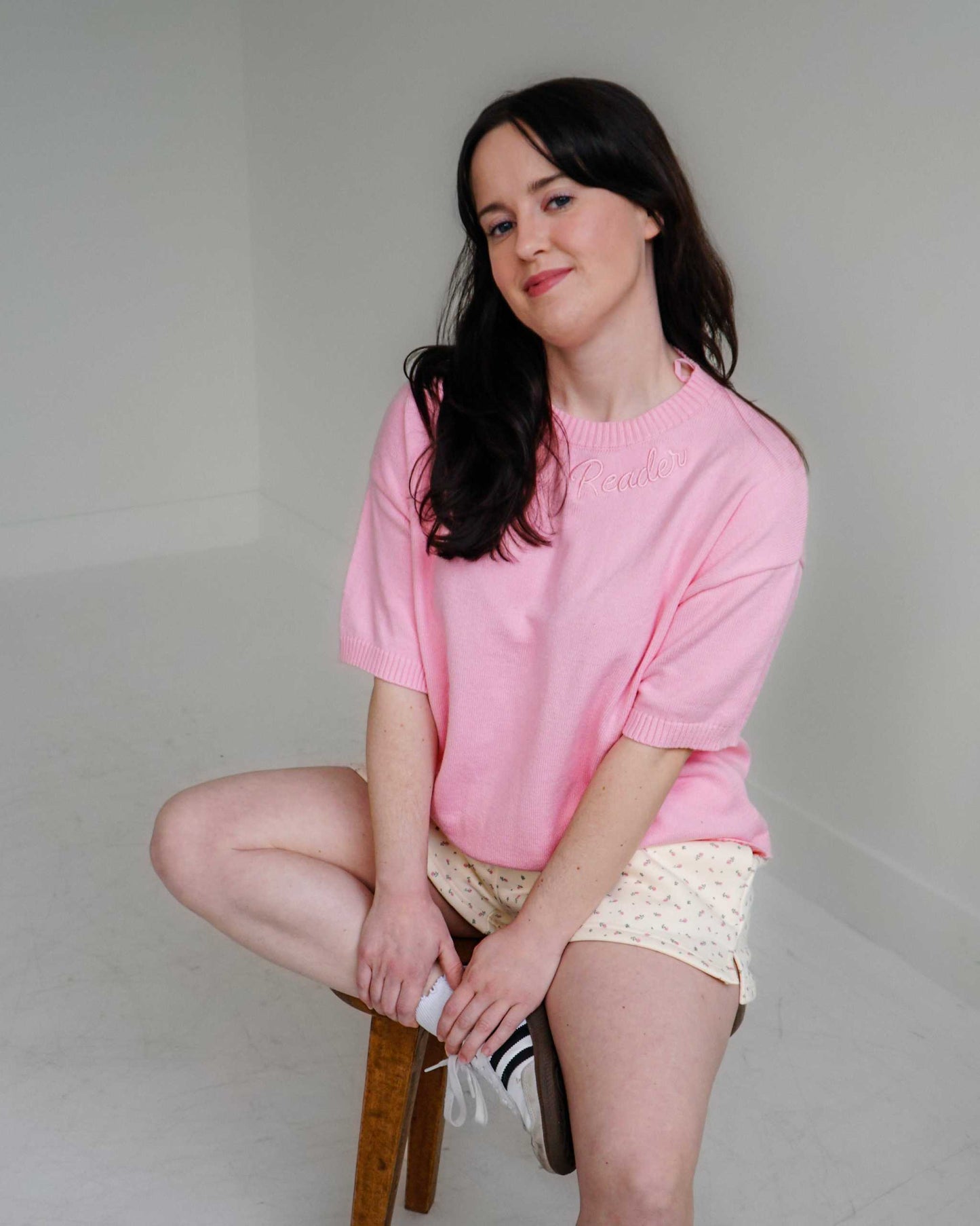 Woman wearing a cozy pink Reader Knit Sweater for book lovers with 'reader' embroidered along the collar. 