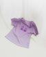 The Book Bears Baby Tee features a design with two teddy bears each holding a book. The t-shirt is a light purple color with a deep purple bookish design and lettuce hem trim.