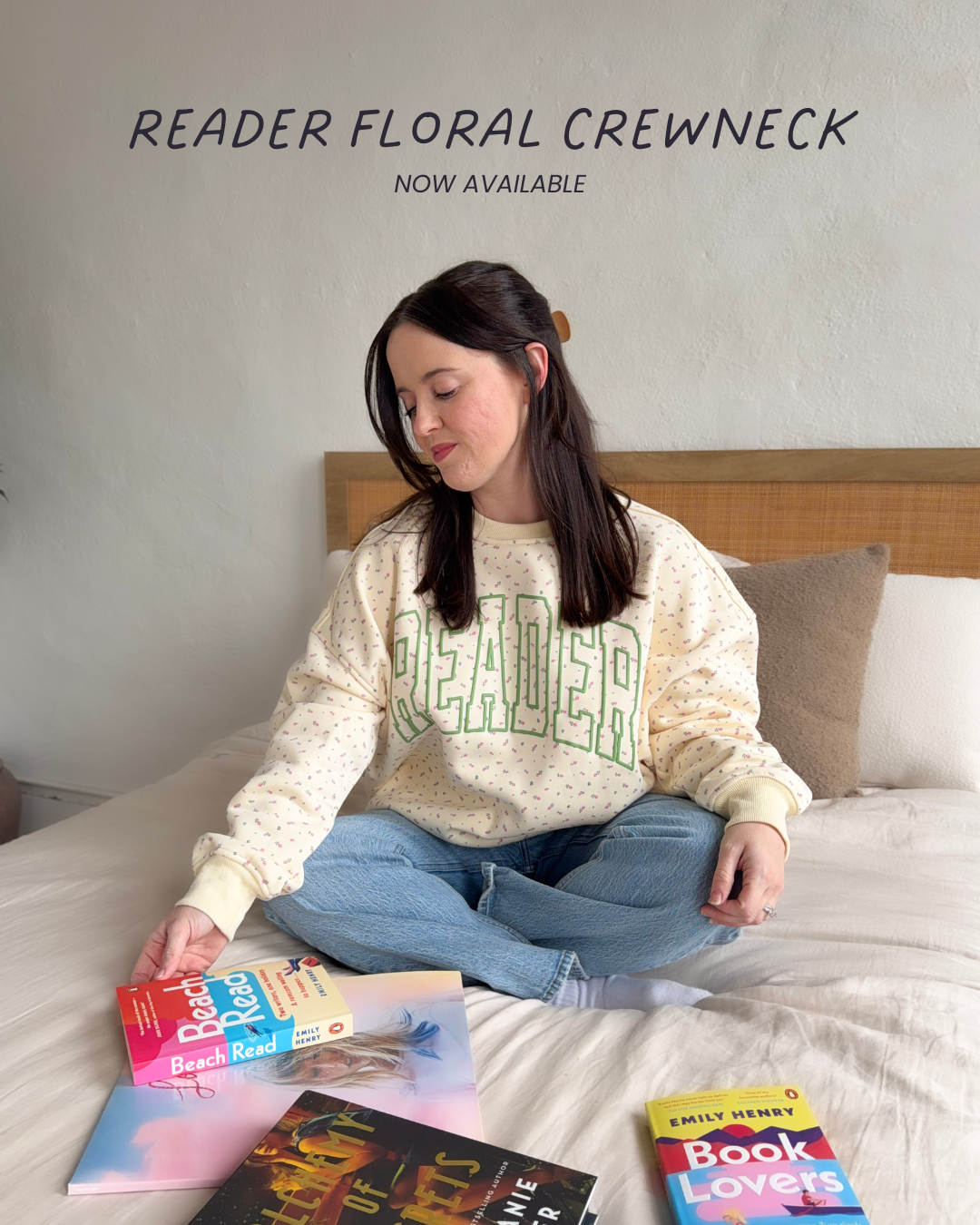 Person wearing a 'Reader' sweatshirt sitting on a bed with books, with text about a 'Reader Floral Crewneck' available.