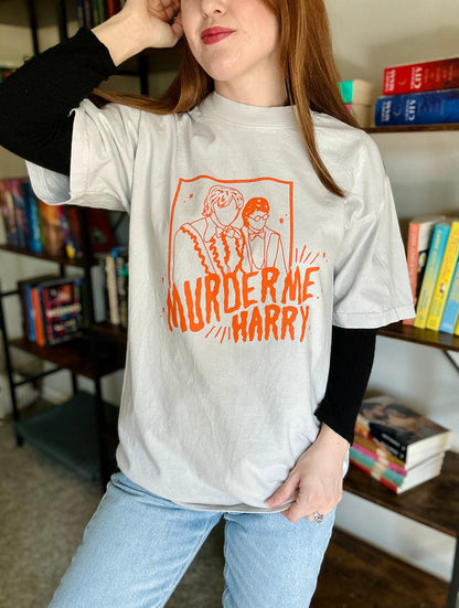 Woman wearing light gray oversized t-shirt with orange "Murder Me Harry" graphic from HP Yule Ball scene