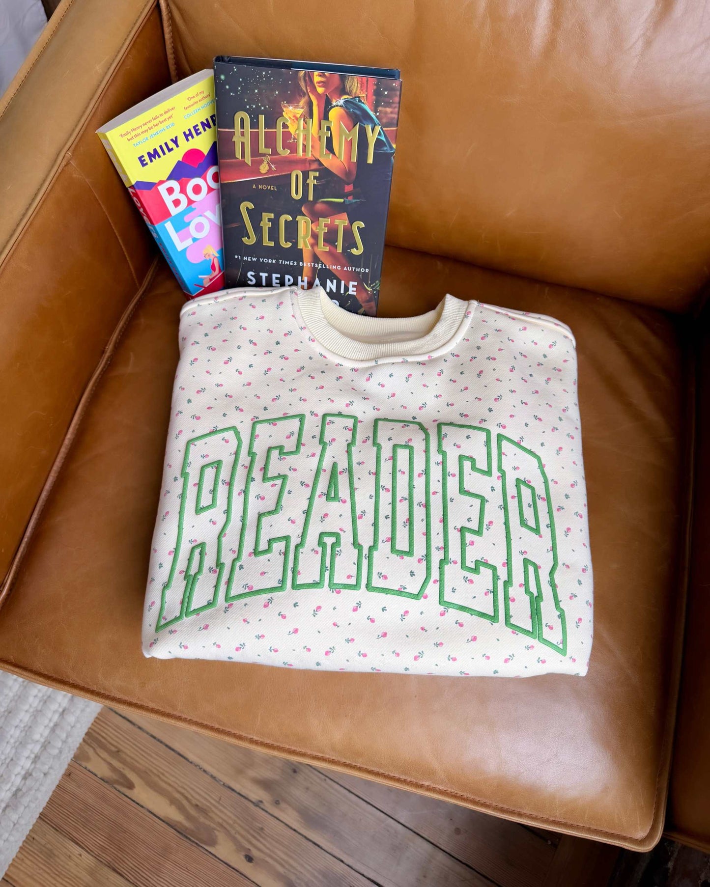 The Reader Floral Crewneck sweatshirt from Next Chapter features a floral pattern with green puff print that says 'Reader' across the front. Next Chapter offers high quality book merch and apparel for readers. 