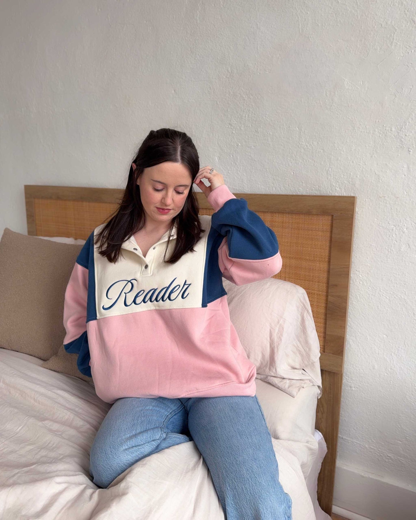 The Reader Colorblock Pullover from Next Chapter is oversized, with a quarter button-up style. This variant is navy, pink, and ivory and has the word 'Reader' embroidered across the front. Next Chapter offers high quality bookish merch and apparel. 
