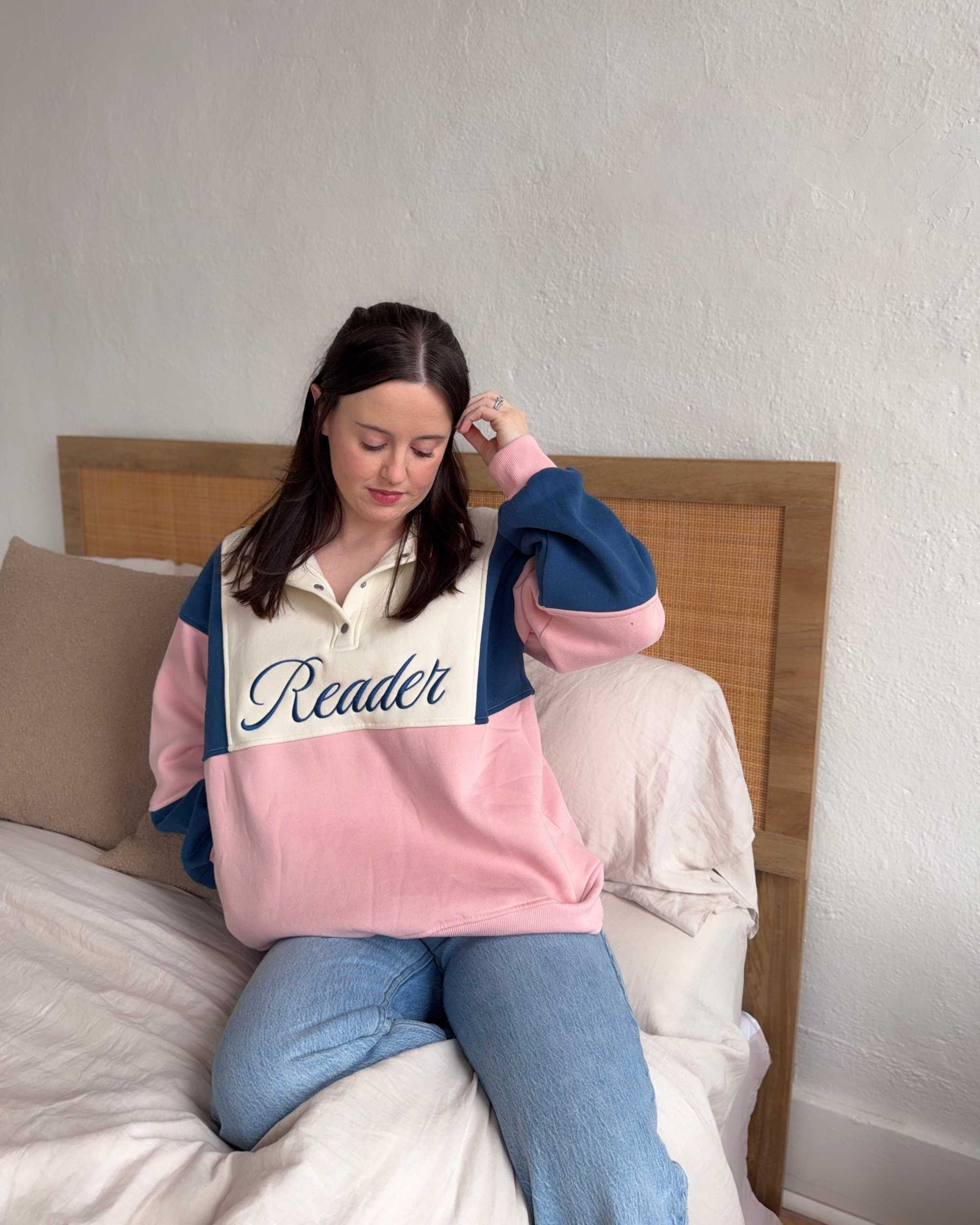 The Reader Colorblock Pullover from Next Chapter is oversized, with a quarter button-up style. This variant is navy, pink, and ivory and has the word 'Reader' embroidered across the front. Next Chapter offers high quality bookish merch and apparel. 