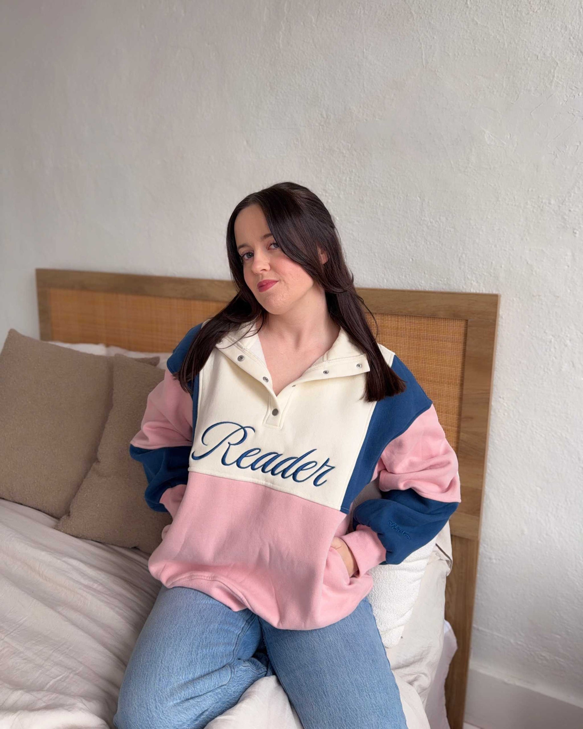 The Reader Colorblock Pullover from Next Chapter is oversized, with a quarter button-up style. This variant is navy, pink, and ivory and has the word 'Reader' embroidered across the front. Next Chapter offers high quality bookish merch and apparel. 
