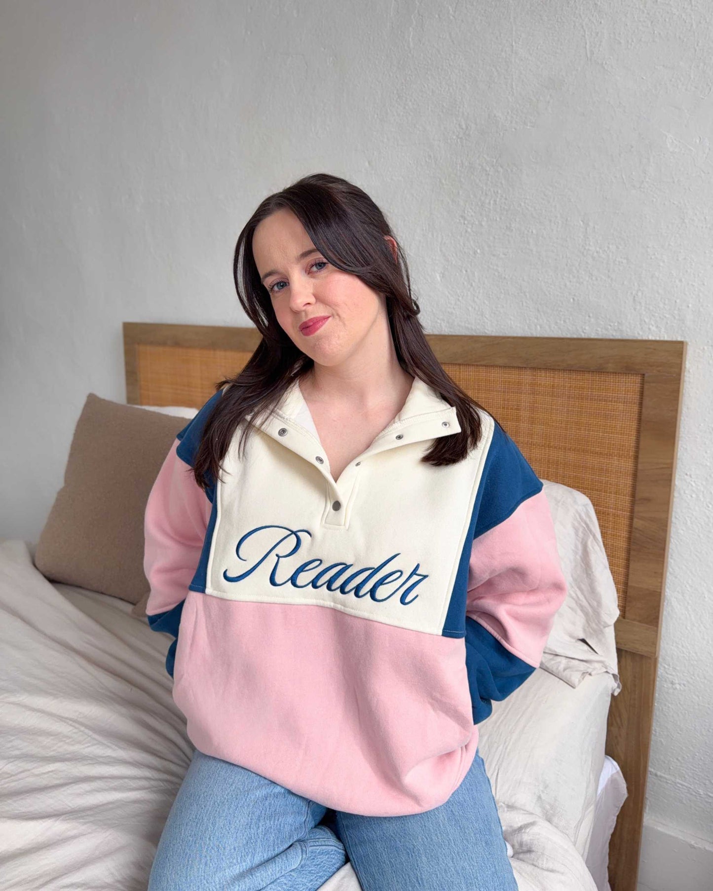 The Reader Colorblock Pullover from Next Chapter is oversized, with a quarter button-up style. This variant is navy, pink, and ivory and has the word 'Reader' embroidered across the front. Next Chapter offers high quality bookish merch and apparel. 
