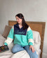 The Reader Colorblock Pullover from Next Chapter is oversized, with a quarter button-up style. This variant is navy, teal, and ivory and has the word 'Reader' embroidered across the front. Next Chapter offers high quality bookish merch and apparel. 