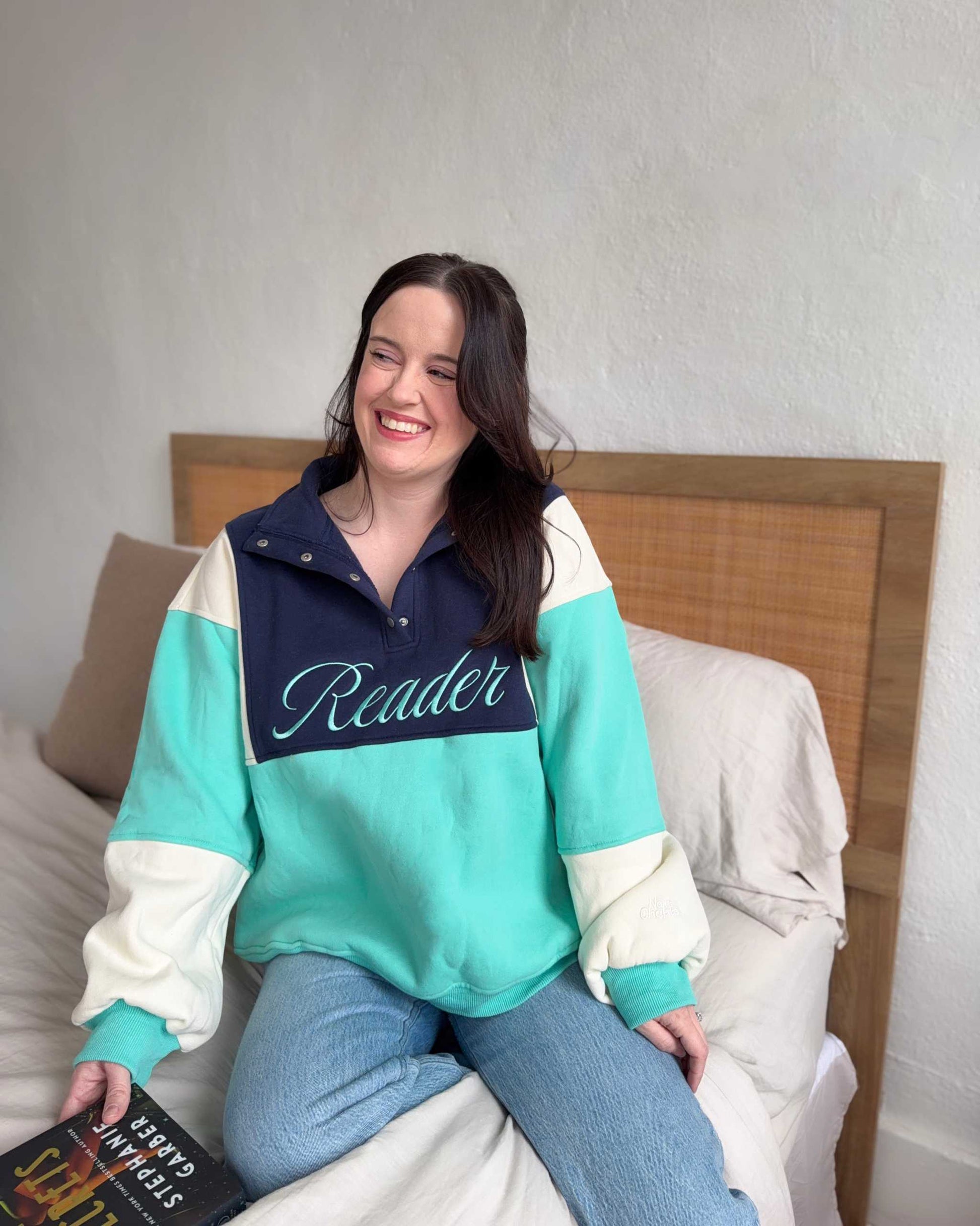 The Reader Colorblock Pullover from Next Chapter is oversized, with a quarter button-up style. This variant is navy, teal, and ivory and has the word 'Reader' embroidered across the front. Next Chapter offers high quality bookish merch and apparel. 