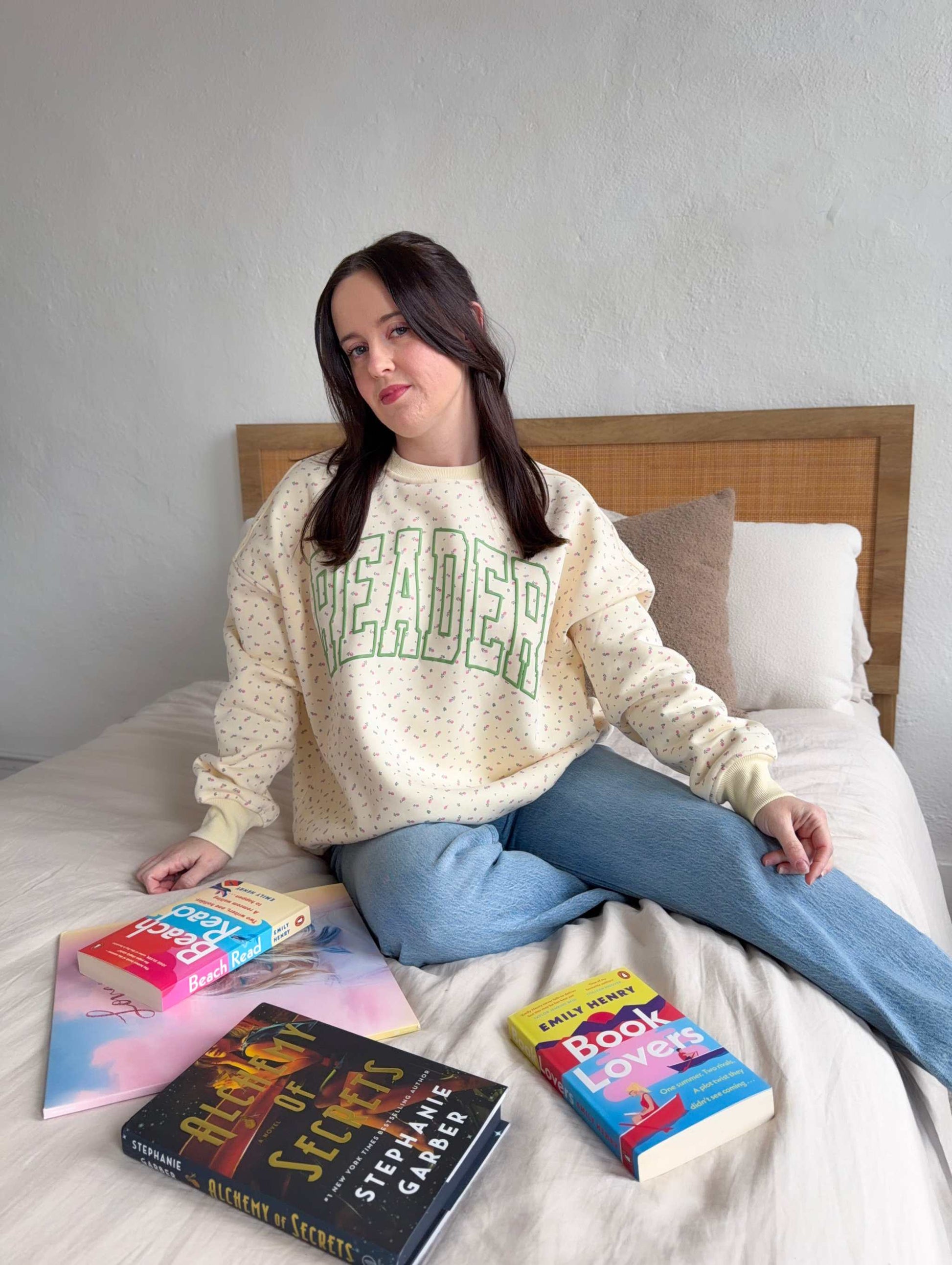 The Reader Floral Crewneck from Next Chapter has a pale yellow fabric with a subtle floral pattern. Across the sweatshirt is the word 'READER' screen printed in green. Next Chapter offers high quality bookish merch and apparel. 