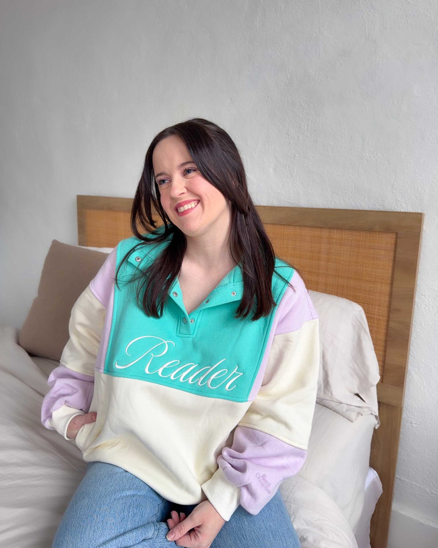 The Reader Colorblock Pullover from Next Chapter is oversized, with a quarter button-up style. This variant is lilac, teal, and ivory and has the word 'Reader' embroidered across the front. Next Chapter offers high quality bookish merch and apparel. 
