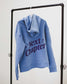 Blue Next Chapter hoodie with 'Next Chapter' puff print text on a black rack against a white background. Next Chapter is a bookish small business that offers officially licensed book merch, including Rachel Gillig merch and Lyla Sage merch.