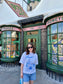 A woman stands outside Honeydukes wearing a t-shirt that depicts the Wizarding World of Harry Potter theme park. The t-shirt also references Taylor Swift's song "Florida!!!" as well as the opening date of the park. 