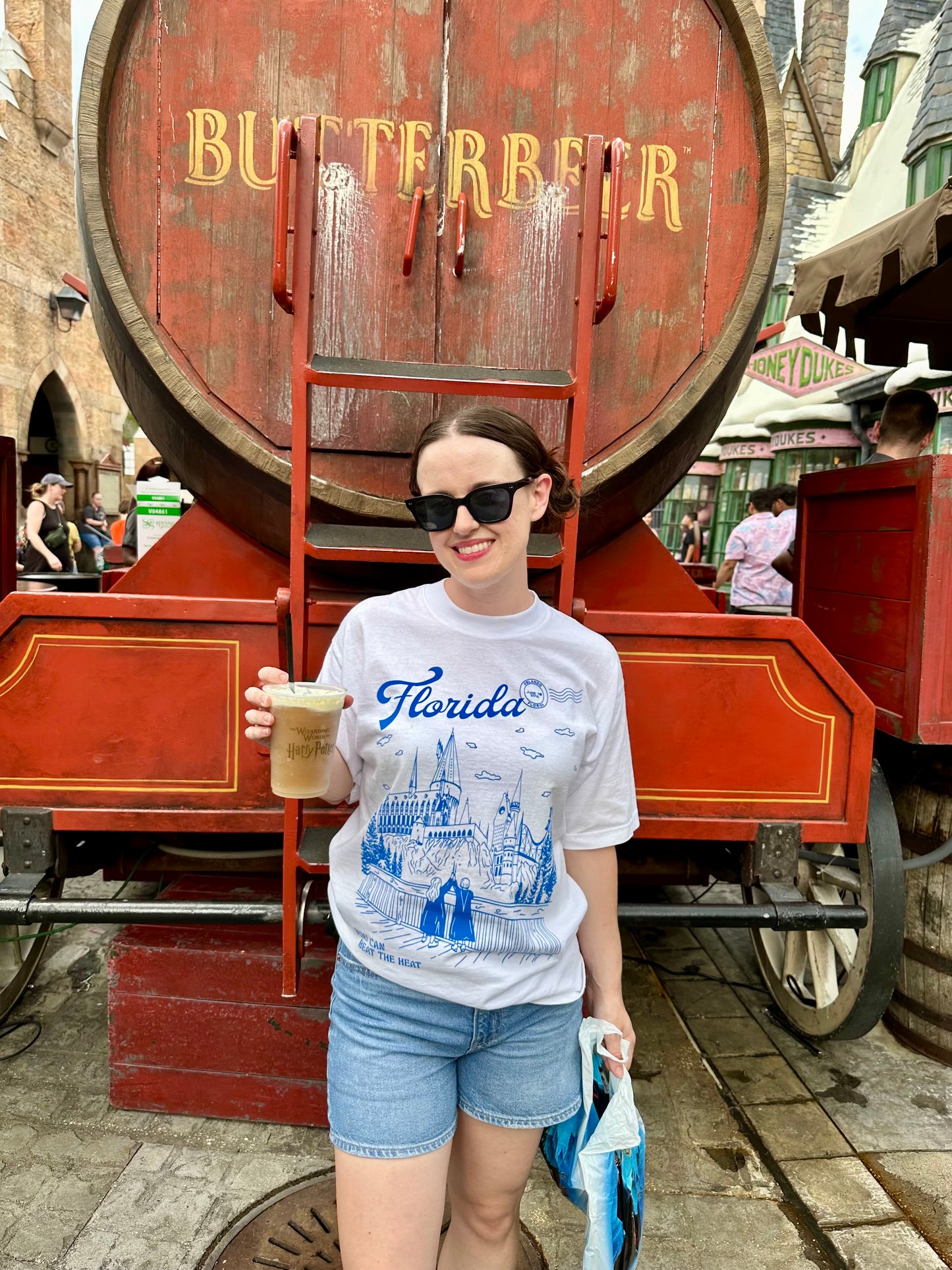 A person at the Wizarding World of Harry Potter holds a butterbeer and wears a t-shirt that depicts theme park. The t-shirt also references Taylor Swift's song "Florida!!!" 