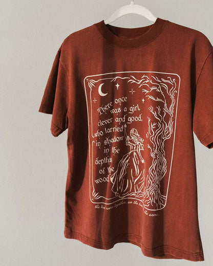 The One Dark Window Tee from Next Chapter is officially licensed by Rachel Gillig and inspired by the Shepherd King Duology. Next Chapter is an official retailer of Rachel Gillig licensed merchandise. This image shows the One Dark Window Tee in the maroon color option.