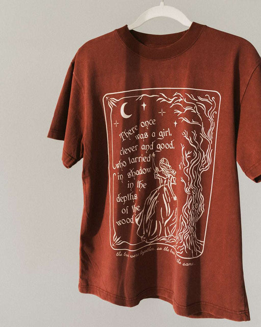 The One Dark Window Tee from Next Chapter is officially licensed by Rachel Gillig and inspired by the Shepherd King Duology. Next Chapter is an official retailer of Rachel Gillig licensed merchandise. This image shows the One Dark Window Tee in the maroon color option.
