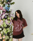 The One Dark Window Tee from Next Chapter is officially licensed by Rachel Gillig and inspired by the Shepherd King Duology. Next Chapter is an official retailer of Rachel Gillig licensed merchandise. This image shows a model wearing the One Dark Window Tee in the maroon color option.