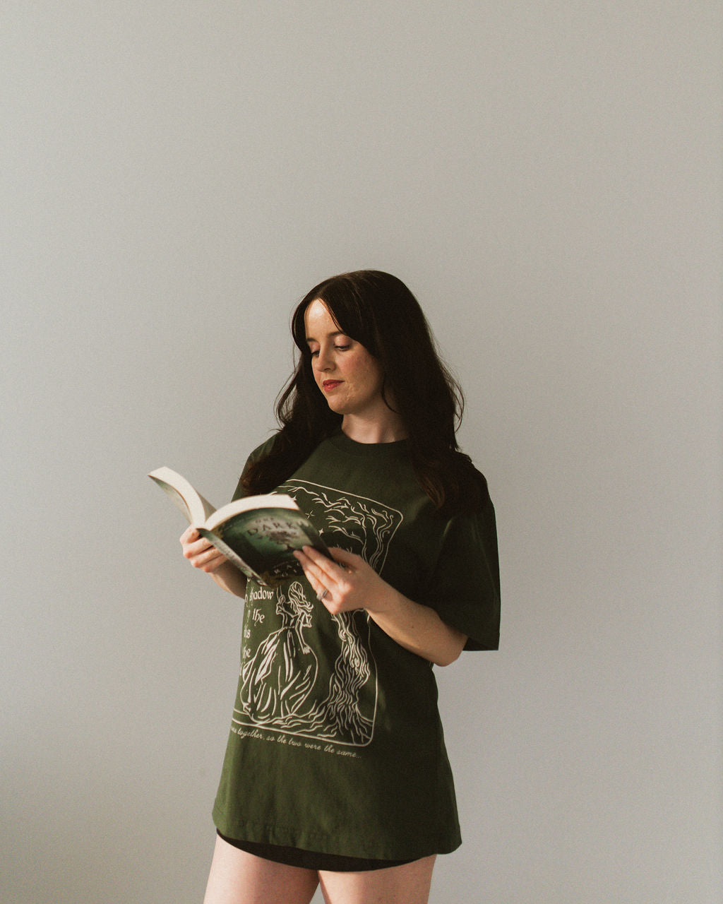 The One Dark Window Tee from Next Chapter is officially licensed by Rachel Gillig and inspired by the Shepherd King Duology. Next Chapter is an official retailer of Rachel Gillig licensed merchandise. This image shows a model wearing the One Dark Window Tee in the green color option.