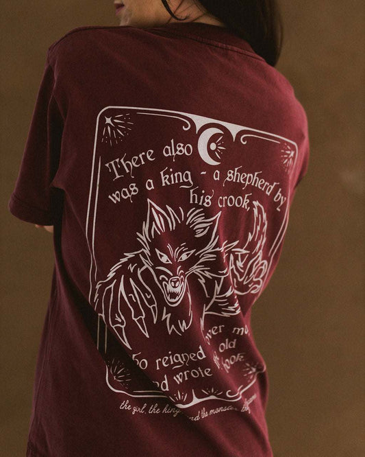 The One Dark Window Tee from Next Chapter is officially licensed by Rachel Gillig and inspired by the Shepherd King Duology. Next Chapter is an official retailer of Rachel Gillig licensed merchandise. This image shows the back design of the One Dark Window Tee in the maroon color option.