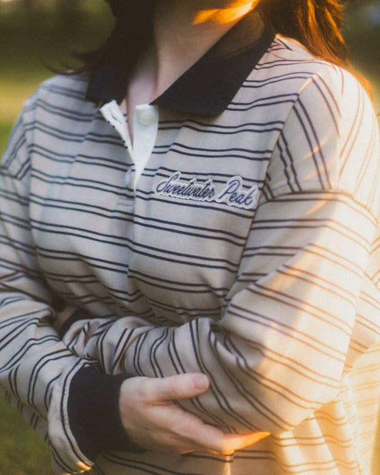 Person wearing a striped shirt with 'Sweetwater Peak' text, sunlit background. A Sweetwater Peak Rugby Top inspired by the book Soul Searching by Lyla Sage. Officially licensed by Lyla Sage.