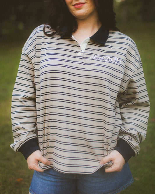Person wearing a striped long-sleeve shirt with a Sweetwater Peak logo in an outdoor setting. A Sweetwater Peak Rugby Top inspired by the book Soul Searching by Lyla Sage. Officially licensed by Lyla Sage.