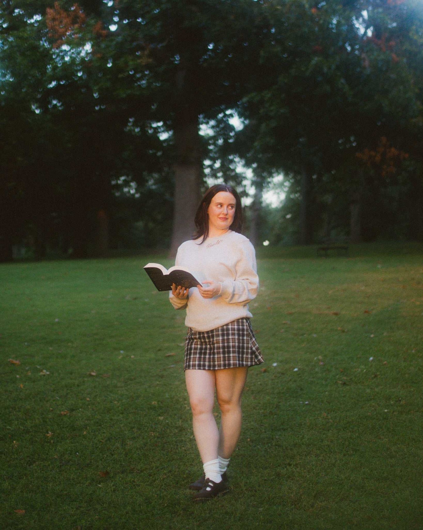 Woman wearing oatmeal beige Reader Embroidered Sweater with golden brown text outdoors in autumn. The sweater reads "Reader" in embroidery around the collar. 